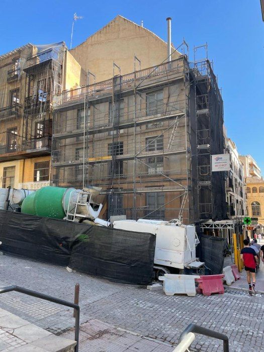 Un edificio en construcción con andamios y una hormigonera verde.