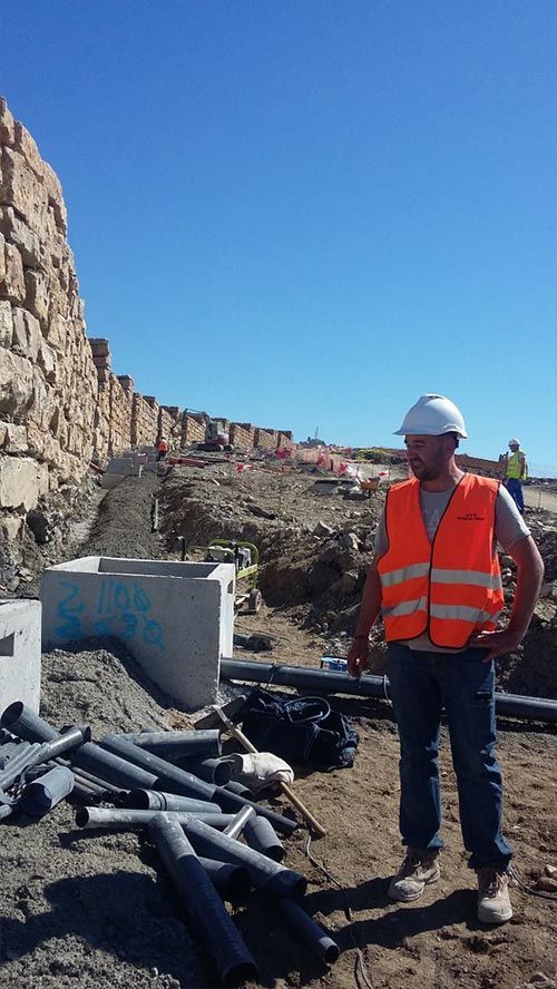 Un hombre con un chaleco naranja y un casco está parado frente a una pila de tuberías.