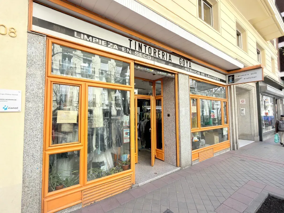 Un local comercial a pie de calle de una tintorería con un marco naranja, una vitrina de cristal y un letrero.