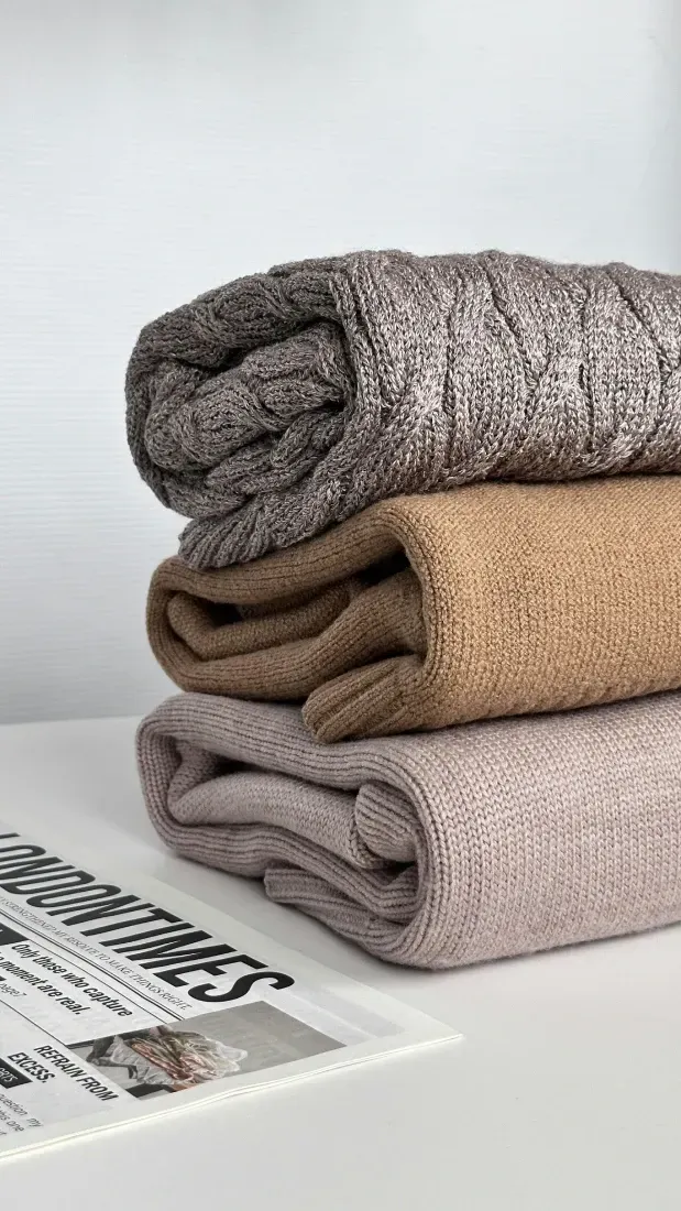 Una pila de tres mantas de punto dobladas en diferentes tonos de marrón y beige.