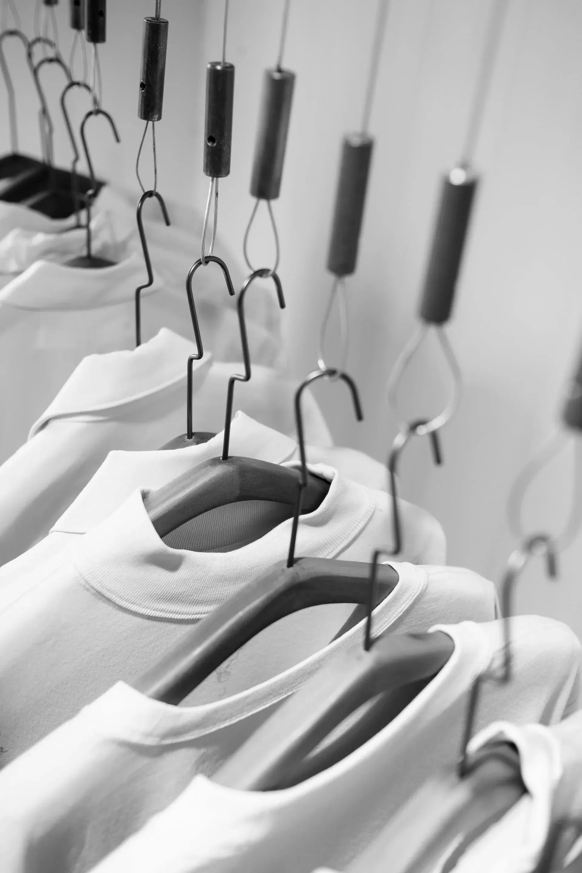 Filas de camisas blancas colgadas en perchas suspendidas de un riel en el techo, en un ambiente limpio y minimalista.
