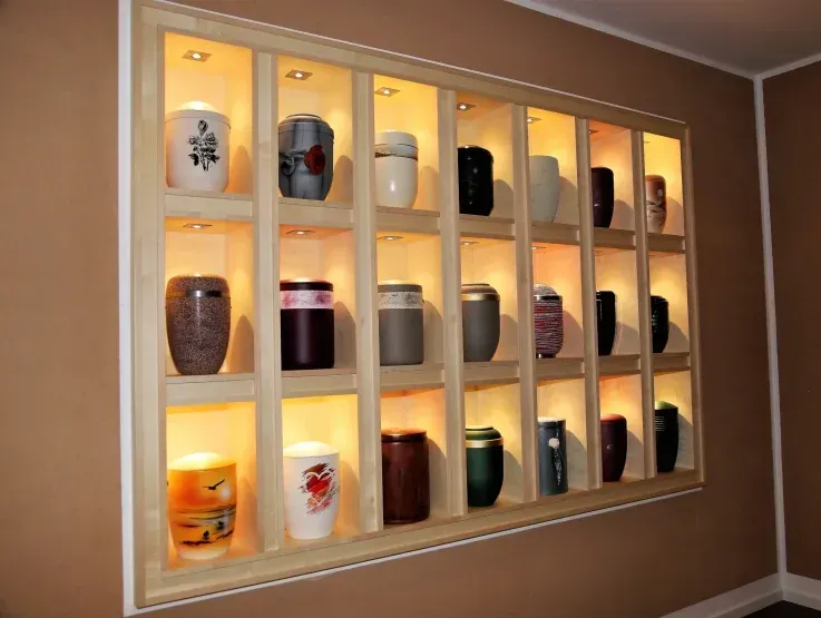 Eine an der Wand befestigte Vitrine mit hinterleuchteten Regalen, in der verschiedene dekorative Urnen ausgestellt sind