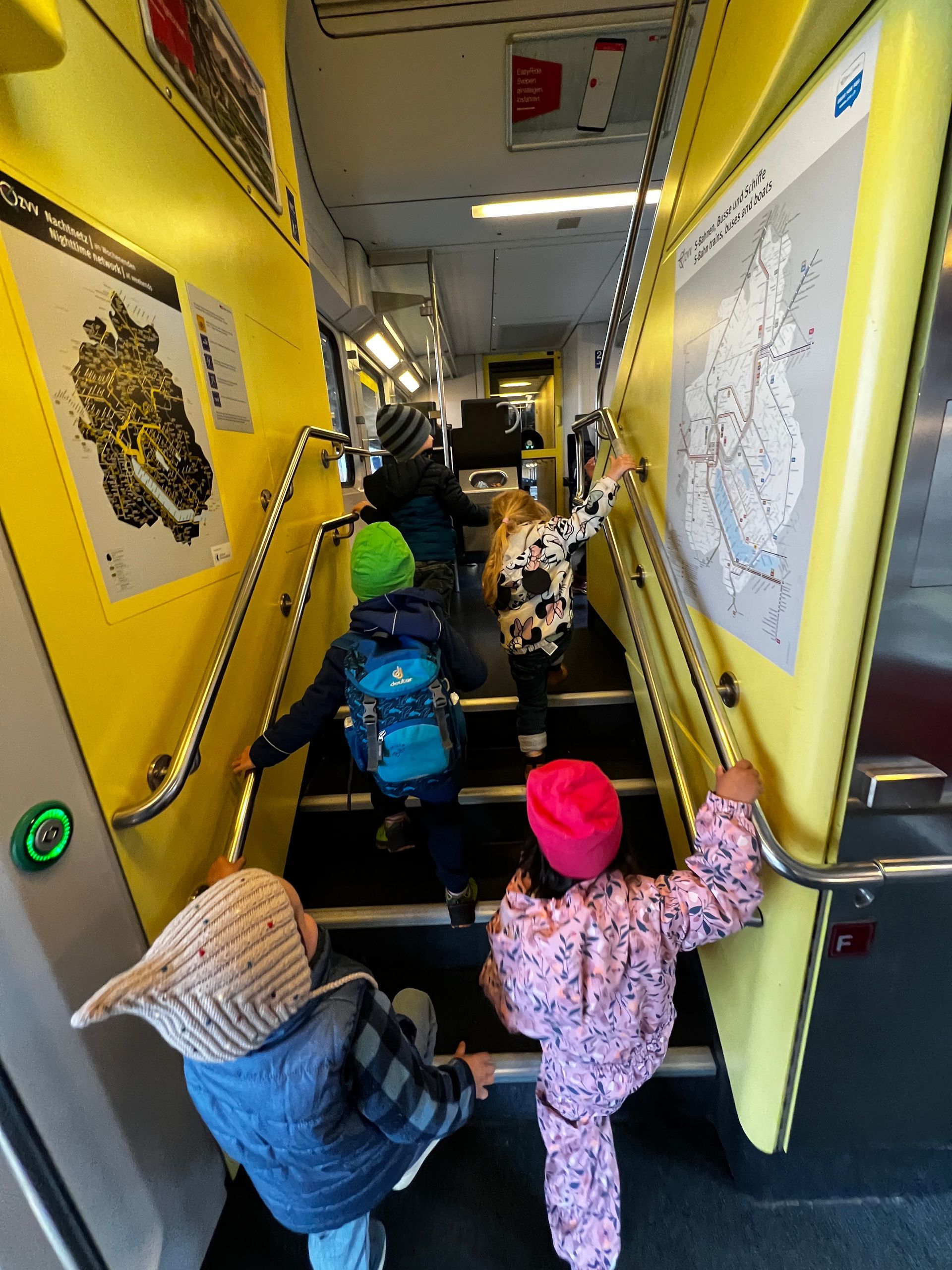 Kinder steigen im Inneren eines gelben Busses Treppen hinauf und halten sich dabei an den Handläufen fest.