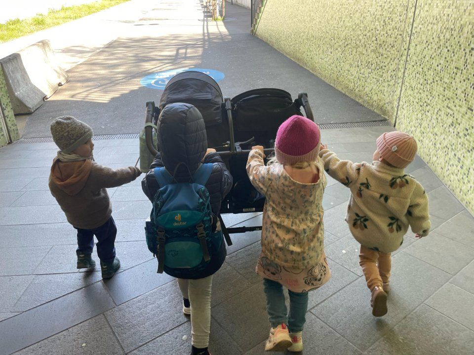 Vier Kinder schieben einen Kinderwagen durch einen Tunnel und halten ihn gemeinsam fest.
