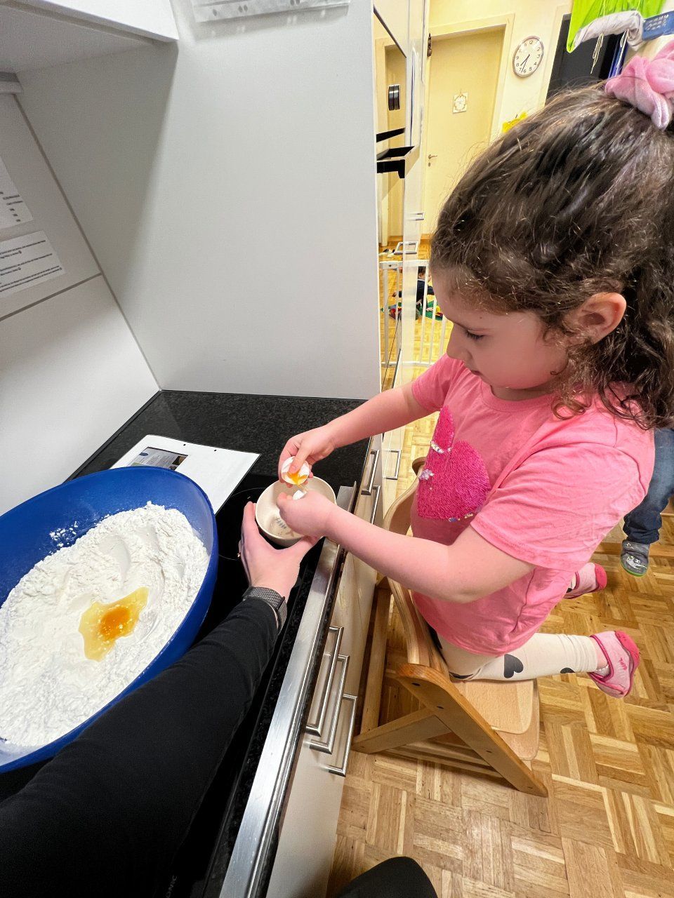 Ein junges Mädchen in einem rosa Hemd schlägt drinnen ein Ei in eine Schüssel mit Mehl.