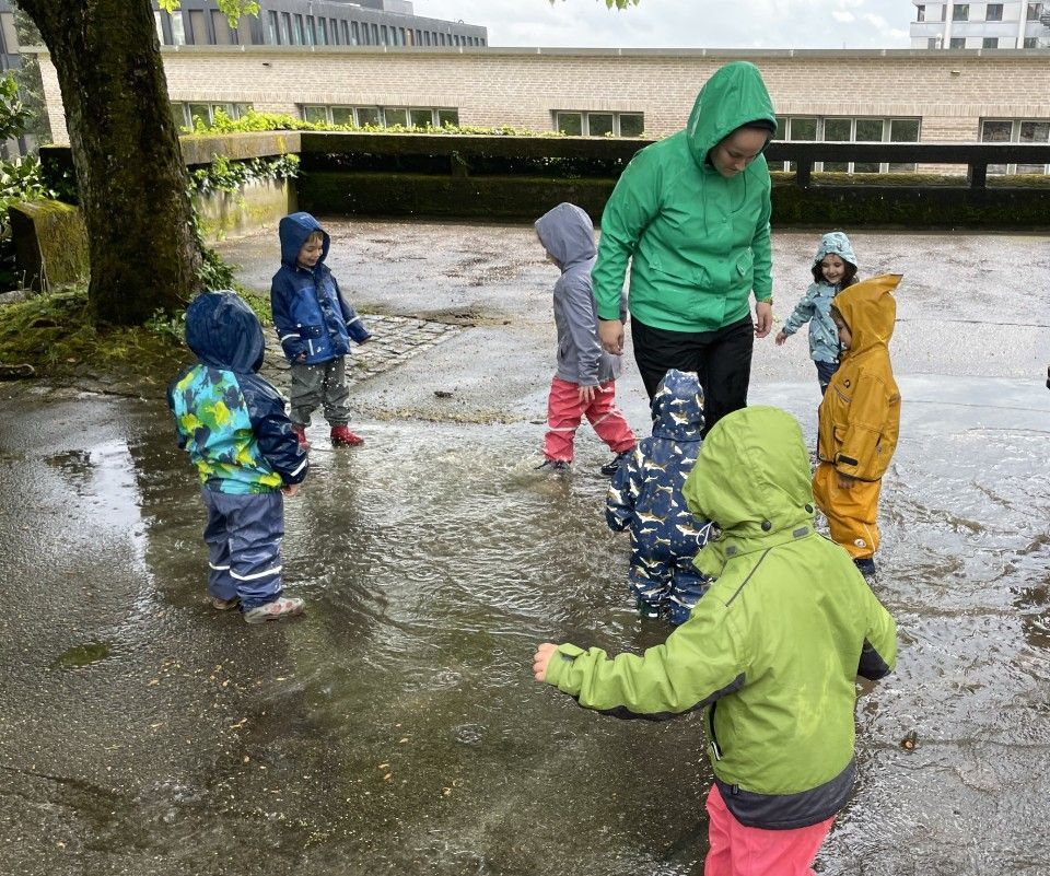 Kinder und Erwachsene in Regenkleidung planschen draußen in Pfützen.