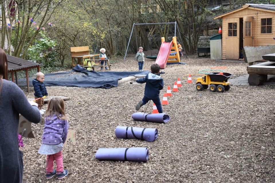 Ein Junge springt auf Matten. Andere spielen in der Nähe von Schaukeln, einer Rutsche und einem Spielzeuglaster.