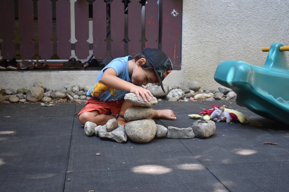 Ein Junge mit Hut stapelt Steine ​​auf einer schwarzen Fläche neben einem grünen Spielgerät.