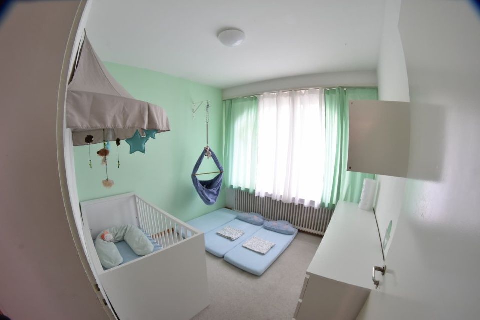 Babyzimmer mit Kinderbett, Hängeschaukel und Kommode; pastellgrüne Wände.