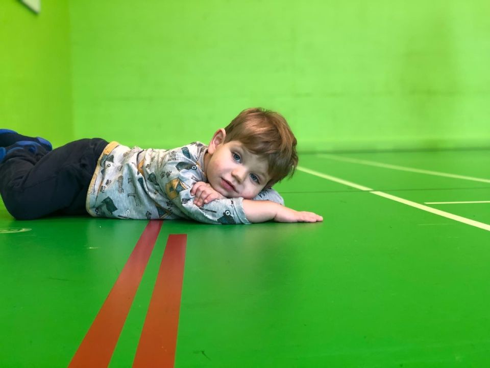 Ein kleines Kind liegt auf einem grünen Boden und schaut in die Kamera.