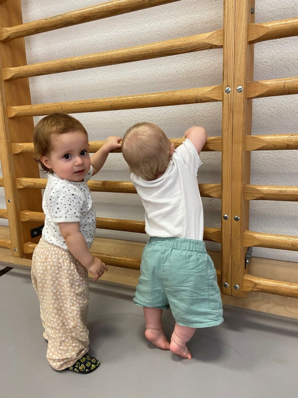 Zwei Kleinkinder halten sich an einem hölzernen Klettergerüst fest.