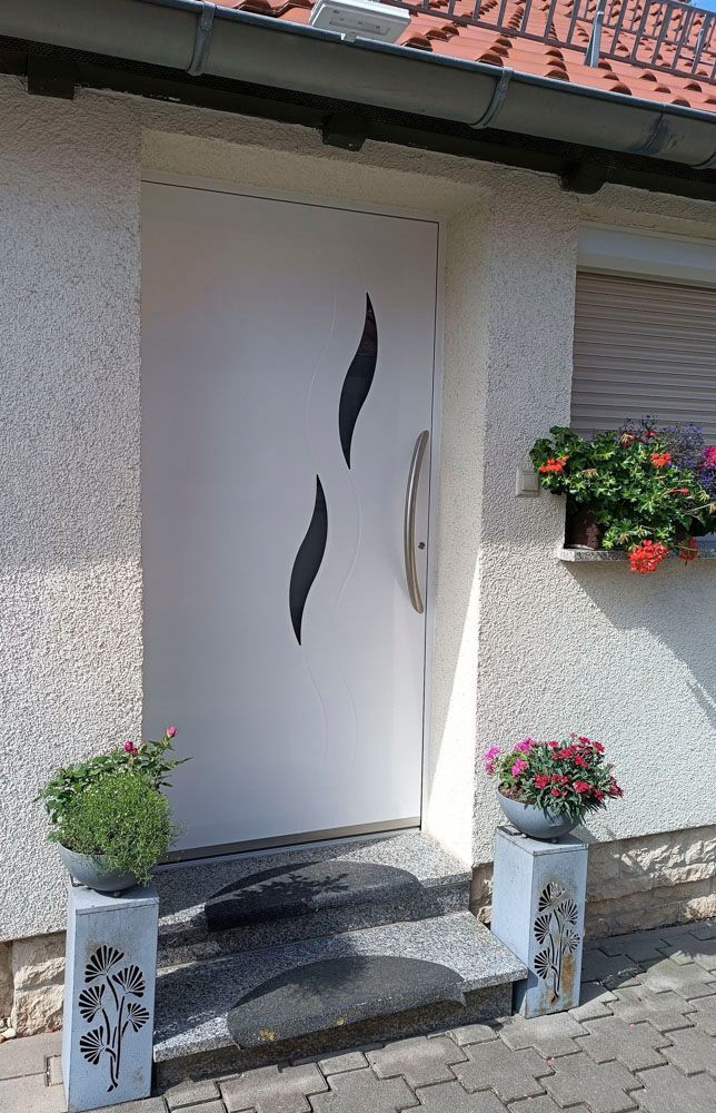 Haustür eines Hauses mit weißen Wänden, schwarzem Zierglas und Blumenkästen an der Treppe