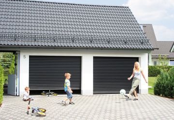 Familie spielt Fußball vor einer Doppelgarage mit schwarzen Rolltoren.