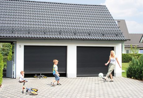 Familie spielt Fußball vor einer Doppelgarage mit schwarzen Rolltoren.