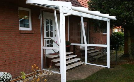 Weiße, mit Fliegengitter versehene Veranda über Ziegelstufen, die zu einer Haustür führen, die an ein Ziegelhaus angebaut ist.