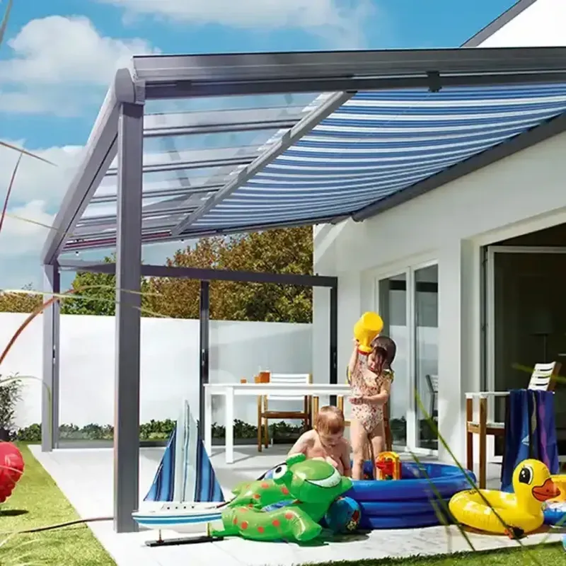 Kinder spielen in einem kleinen Pool unter einer gestreiften Markise, neben einem weißen Haus und einem gedeckten Tisch.