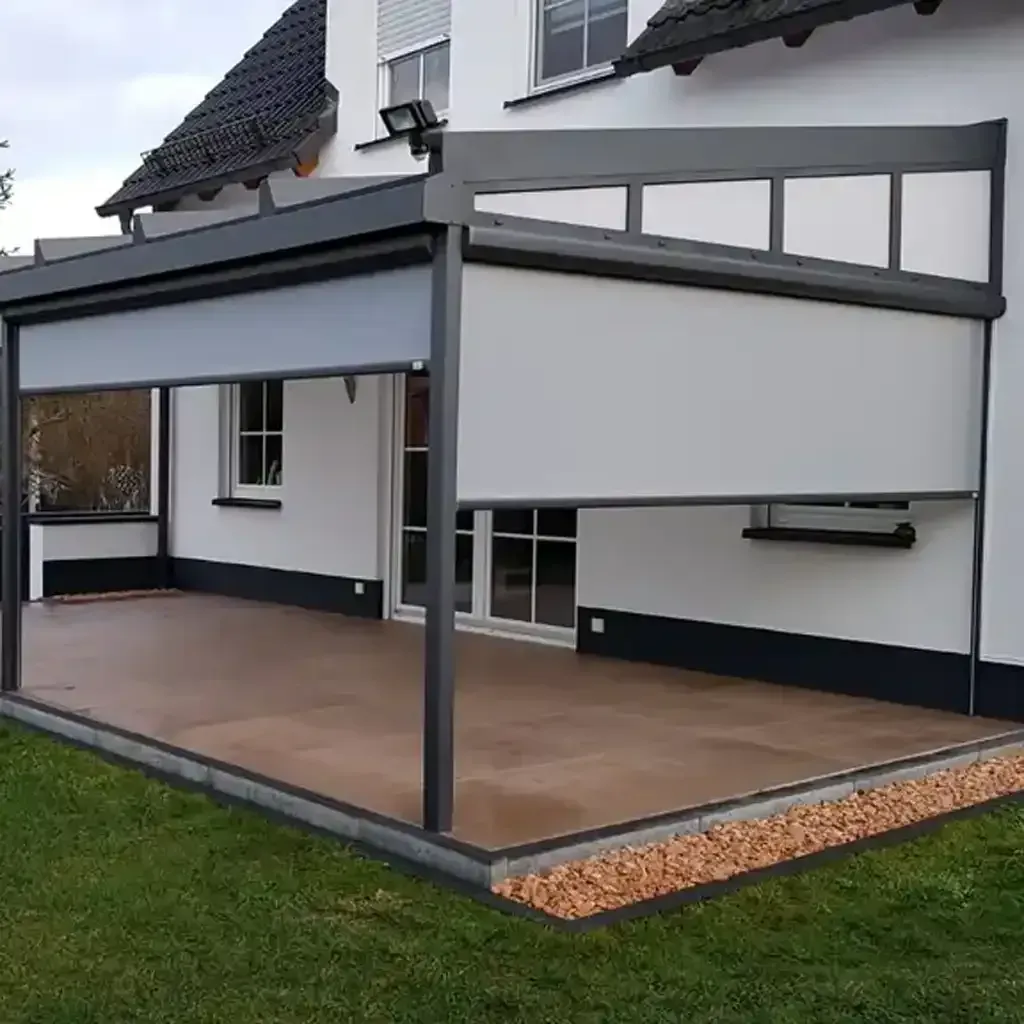 Terrasse mit grauer Markise und hellgrauen Jalousien, neben einem weißen Haus mit grünem Rasen.