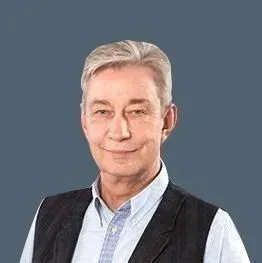 Lächelnder Mann in hellblauem Hemd und schwarzer Weste vor einfarbigem grauen Hintergrund