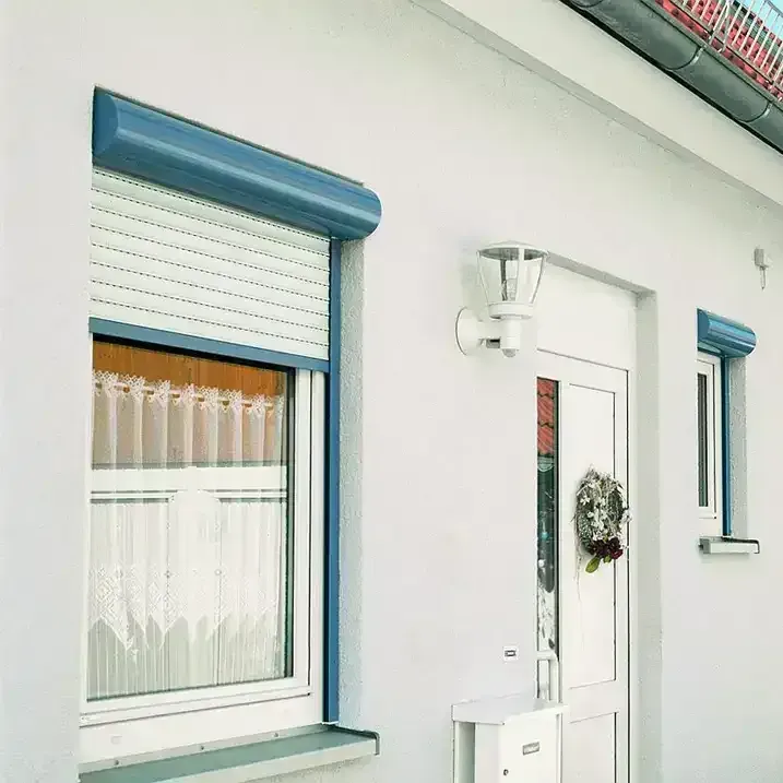 Außenansicht eines weißen Gebäudes mit einem geschlossenen blauen Rollladen über einem Fenster und einer geschlossenen weißen Tür, Leuchte.
