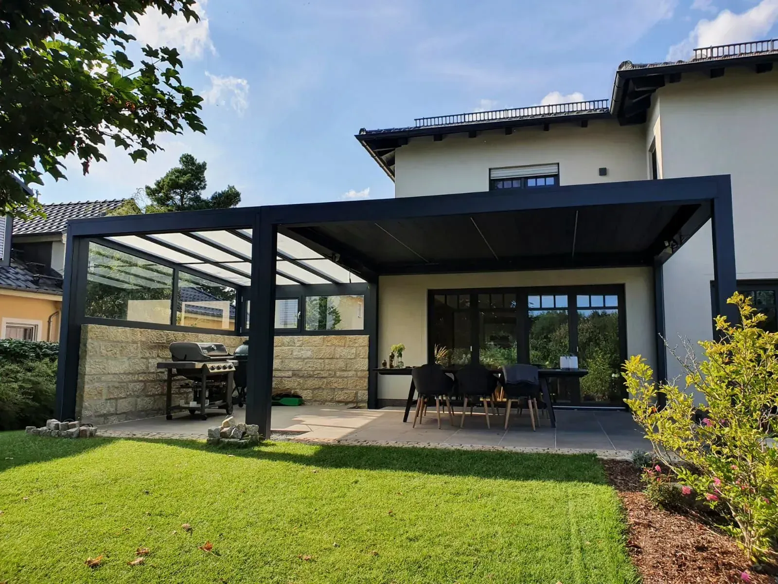 Moderne Hausterrasse mit dunkler Pergola, Esstisch im Freien und grünem Rasen