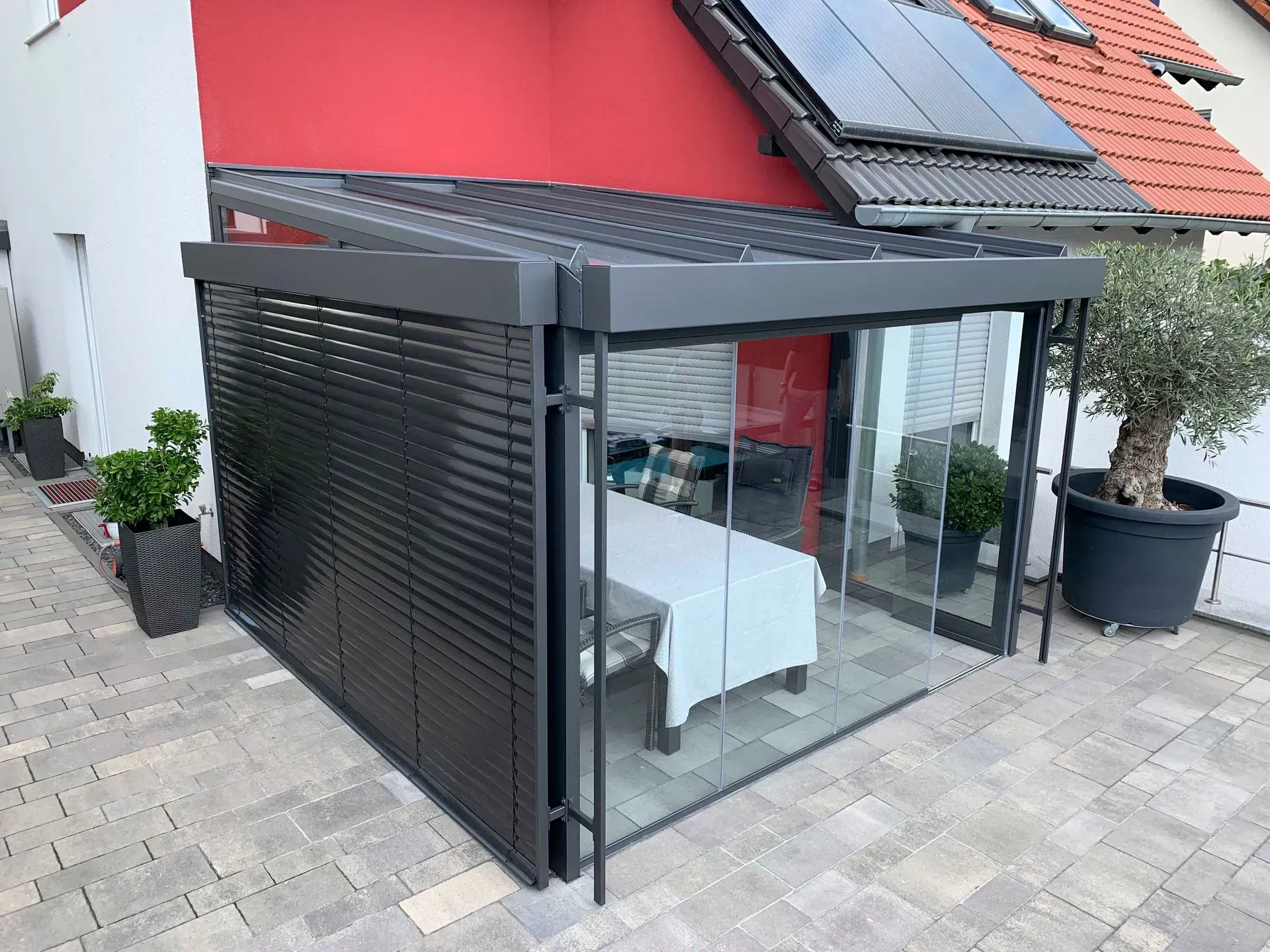 Schwarze, metallgerahmte Glasterrasse neben einem Haus mit roten Dachziegeln