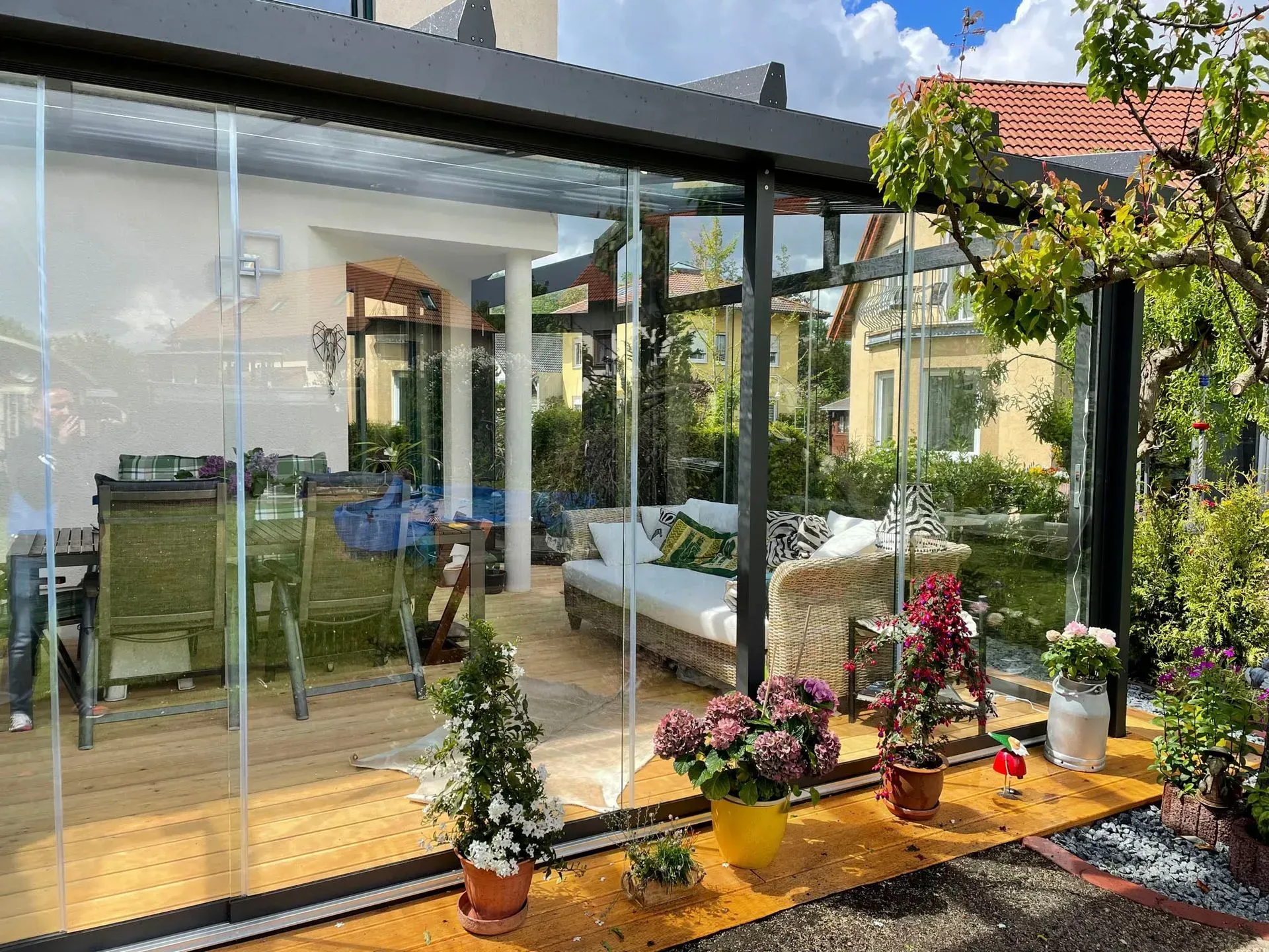 Verglaste Terrasse mit Topfblumen, Sitzgelegenheiten im Freien und Gartenblick im hellen Sonnenlicht