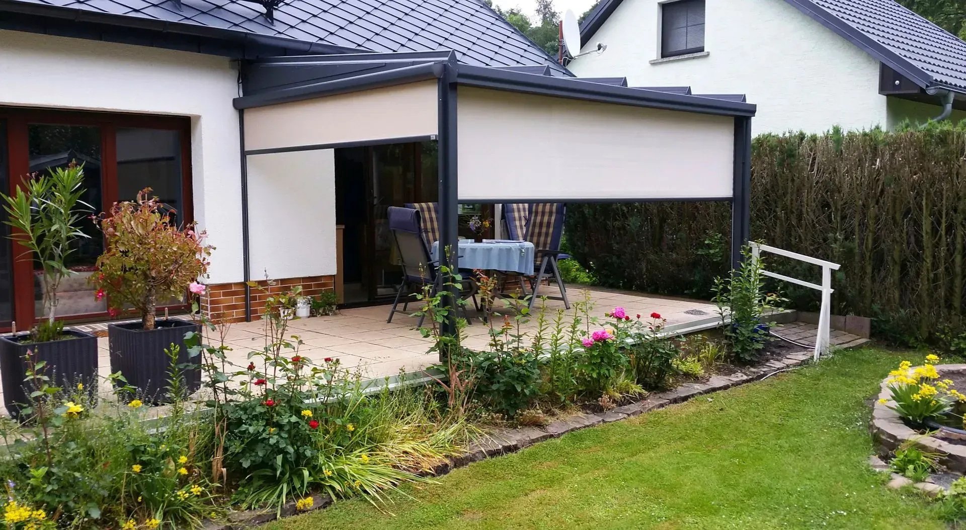 Moderne Hausterrasse mit Pergola, Blumenbeeten und gepflegtem Rasen