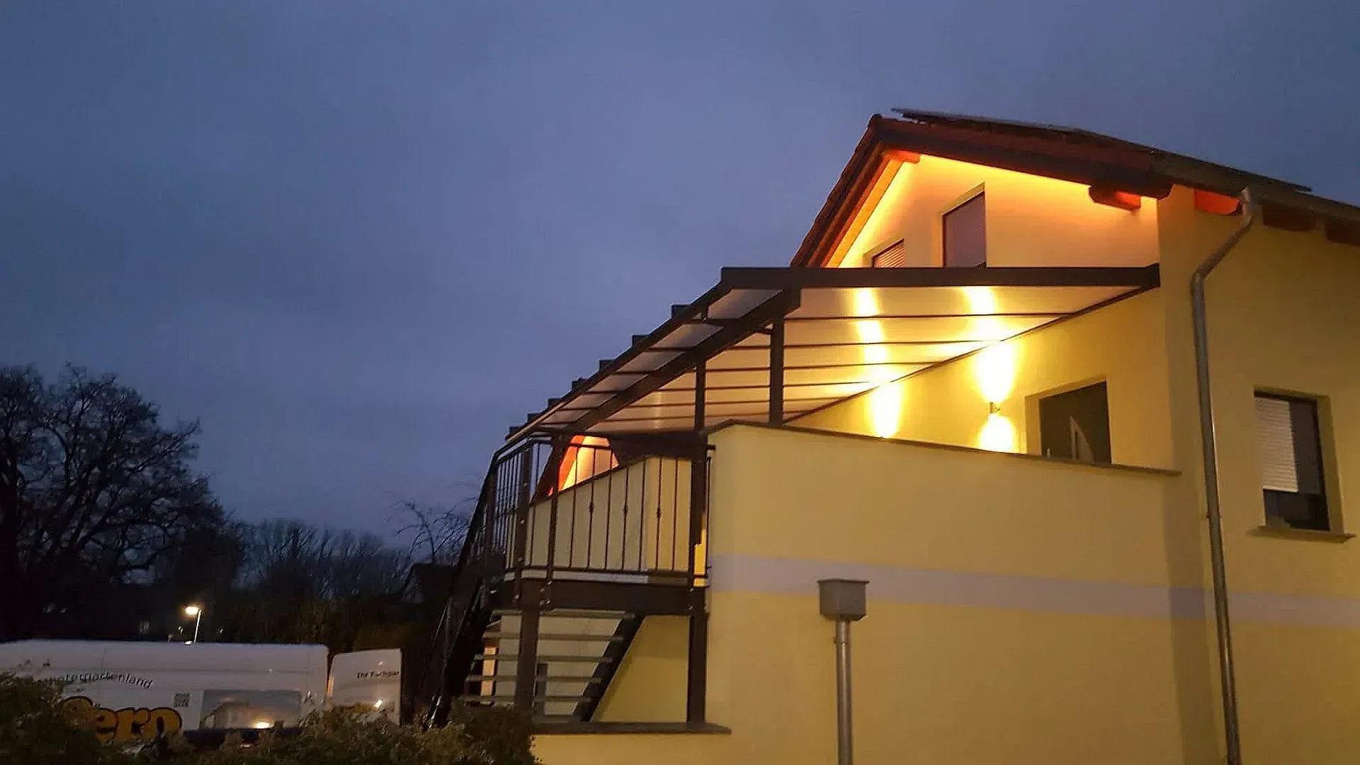 Gelbes Haus in der Abenddämmerung mit beleuchteten Balkonen und Treppen, von der Seite unter einem dunklen Abendhimmel gesehen