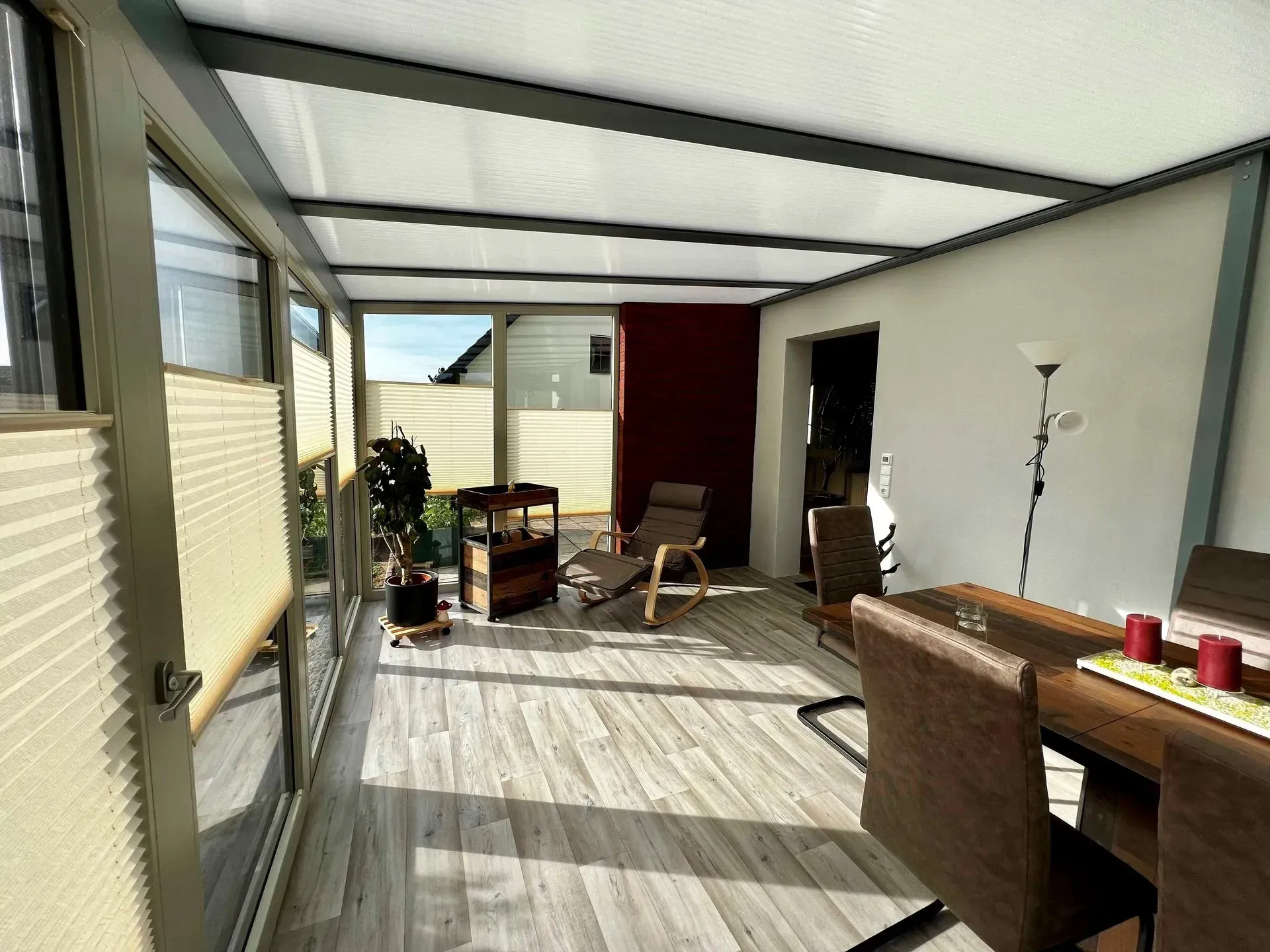 Überdachte Terrasse mit Korbstühlen, Esstisch und Grill im hellen Sonnenlicht