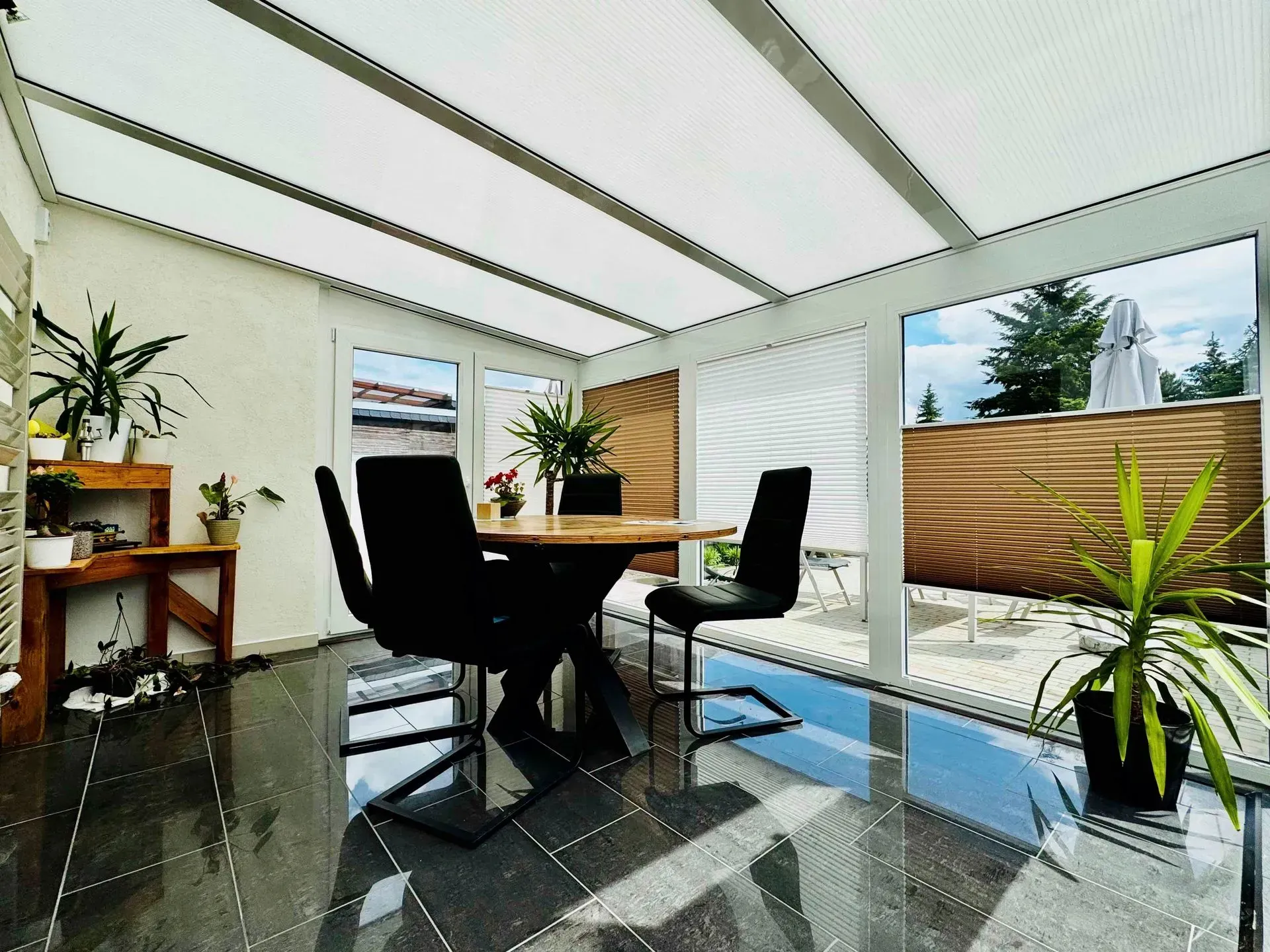 Moderner Wintergarten mit schwarzen Stühlen, Holztisch, Topfpflanzen und großen Fenstern mit Blick auf Terrasse und Garten