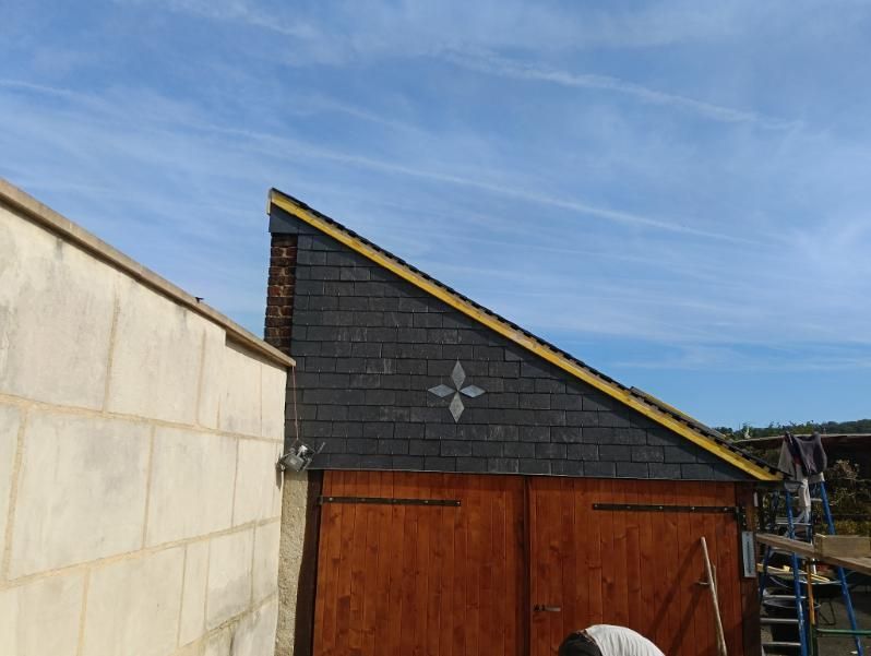 Un mur d'abri en pente, recouvert de carreaux sombres et orné d'un emblème décoratif en forme d'étoile à quatre, se trouve à côté d'un mur de maçonnerie.