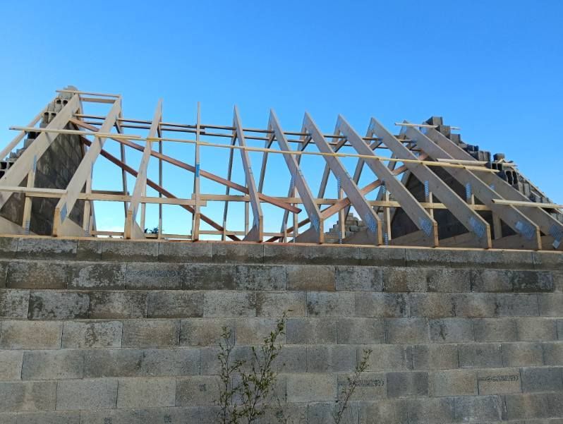 Une charpente de toit en bois en construction, avec des chevrons reposant sur un mur de briques de pierre.