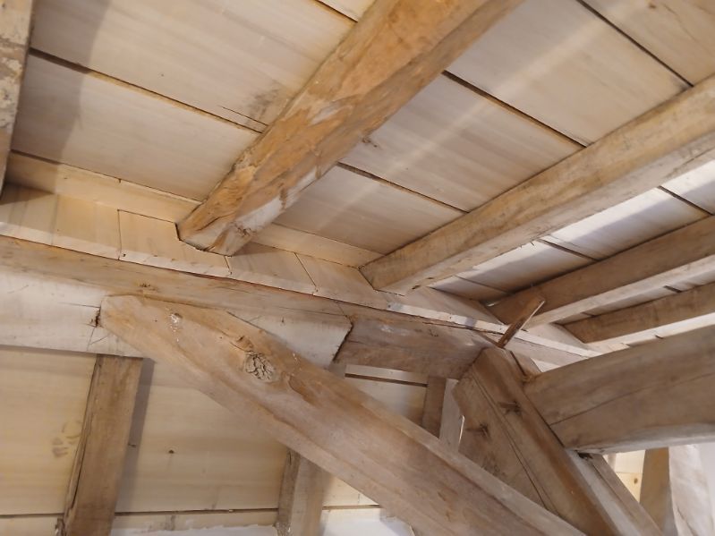 Vue en contre-plongée de poutres en bois brut et de planches de plafond, montrant la construction d'une toiture ou d'une charpente.