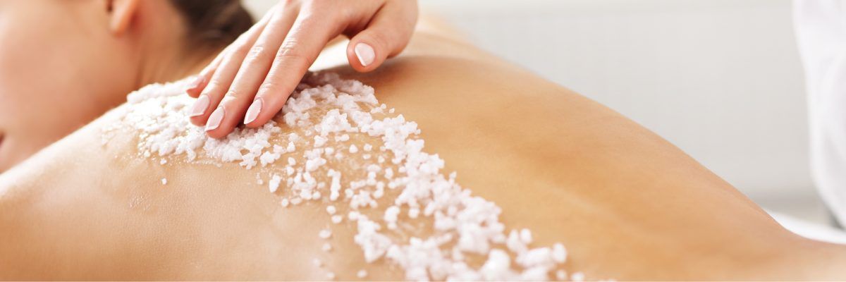 Een persoon die een rugscrubbehandeling krijgt in een spa, waarbij met een hand voorzichtig een korrelige substantie wordt aangebracht.