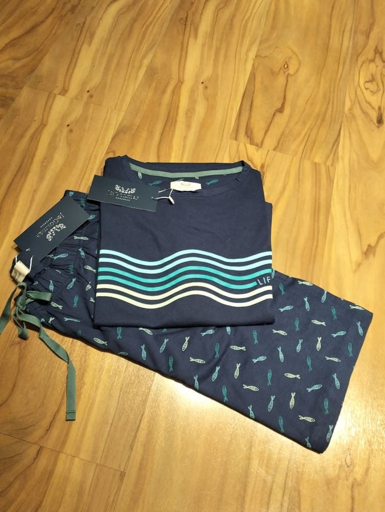 Un conjunto de pijama azul marino doblado, con un estampado de olas en la camisa y un pequeño estampado de peces en el pantalón, sobre un suelo de madera.