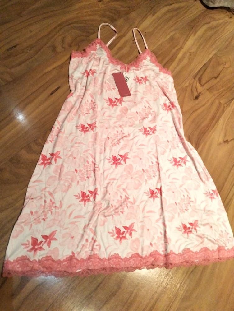 Un camisón blanco de tirantes con estampado floral rosa, ribete de encaje en el escote y el bajo, y una etiqueta de la marca sobre un suelo de madera.
