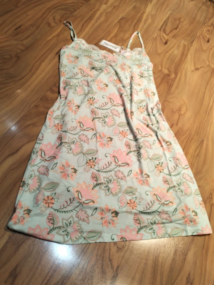 Un vestido lencero de tirantes finos con estampado floral de color claro, expuesto sobre un suelo de madera.