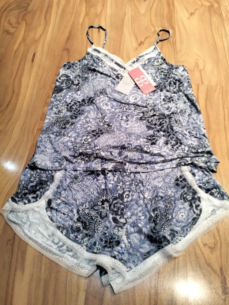 Un conjunto de pijama azul y blanco con estampado floral y ribete de encaje sobre un suelo de madera, compuesto por una camiseta de tirantes y pantalones cortos.