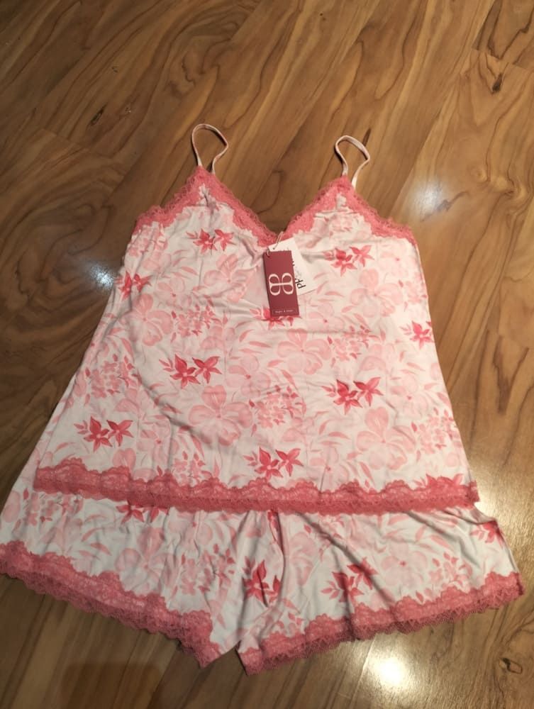 Un conjunto de pijama de dos piezas con estampado floral sobre tela blanca, con ribete de encaje rosa, extendido sobre un suelo de madera.