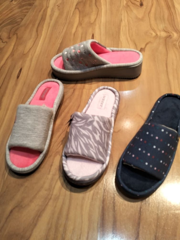 Cuatro sandalias tipo chancla de diferentes colores: gris, rosa, estampado de cebra y lunares azul oscuro, dispuestas sobre una superficie de madera.