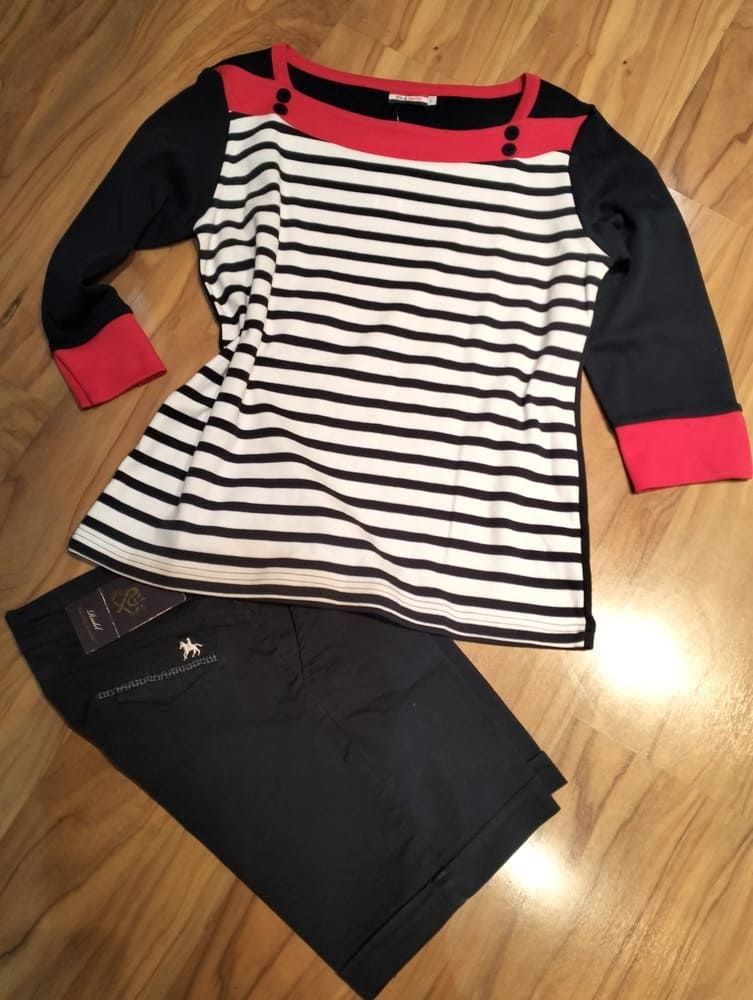 Una camiseta de manga larga a rayas blancas y negras con ribete rojo y un par de pantalones cortos azul oscuro sobre un suelo de madera.