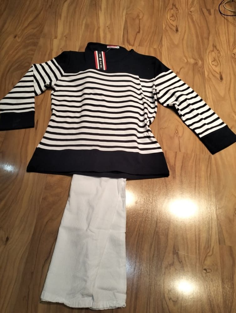 Una camisa de manga larga a rayas azul marino y blancas con una etiqueta roja yacía en el suelo, encima de unos pantalones blancos doblados.