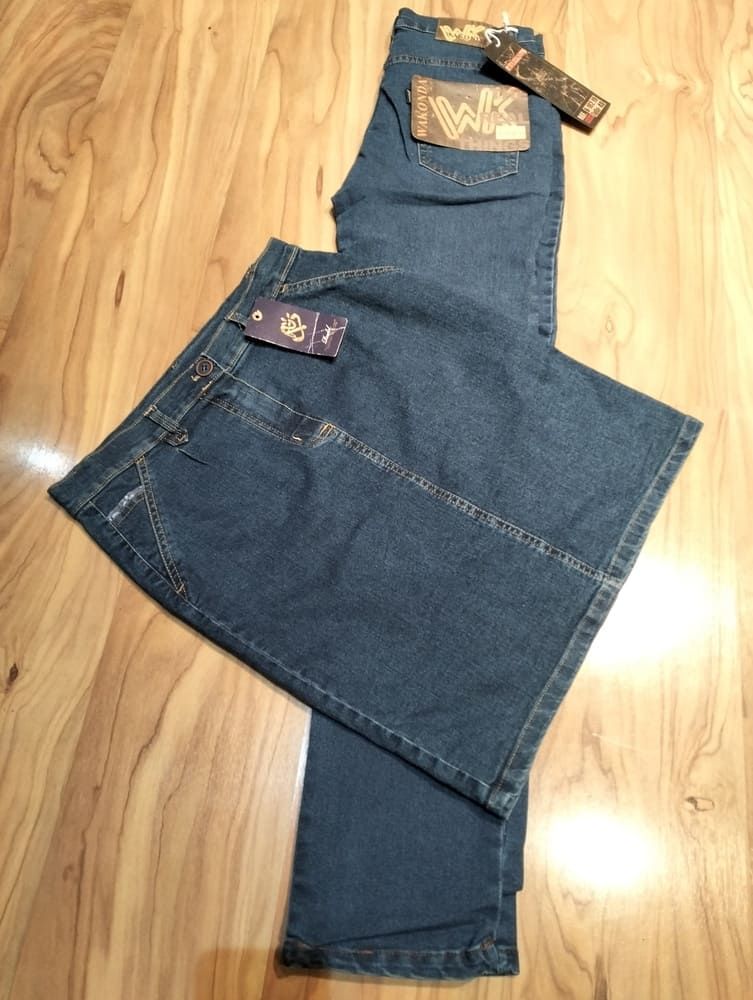 Un par de pantalones vaqueros de mezclilla azul oscuro, con las etiquetas aún puestas, extendidos sobre una superficie de madera de color claro.