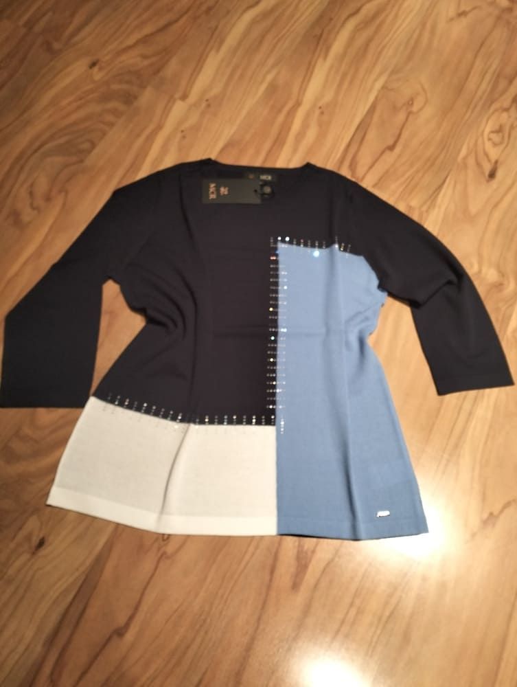 Un suéter de manga tres cuartos con un diseño de bloques de color azul marino, azul claro y blanco roto, con detalles de texto.