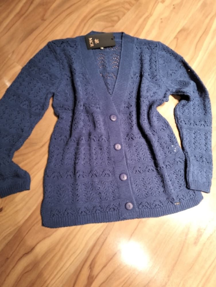 Un cárdigan azul de punto, abotonado y con un delicado estampado que recuerda al encaje, extendido sobre una superficie de madera clara.