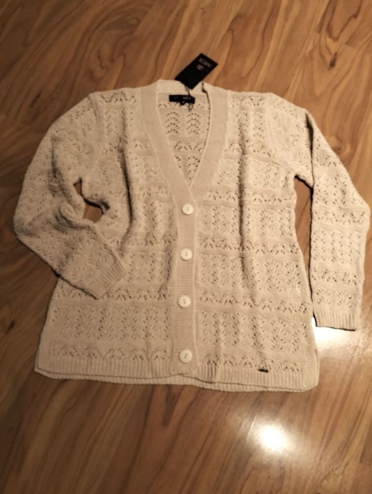 Un cárdigan de punto color crema, con cuello en V y botones, de tejido abierto, extendido sobre un suelo de madera.