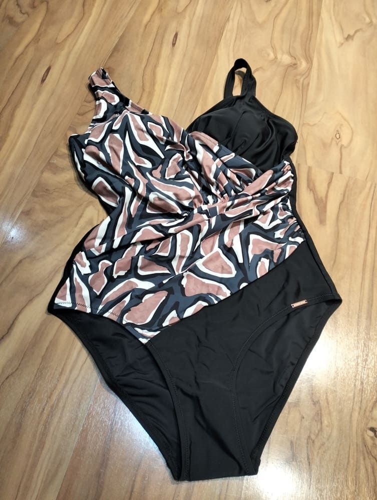 Un bañador de una pieza con la parte inferior negra y un corpiño drapeado con estampado animal abstracto en tonos marrones y negros sobre un suelo de madera.