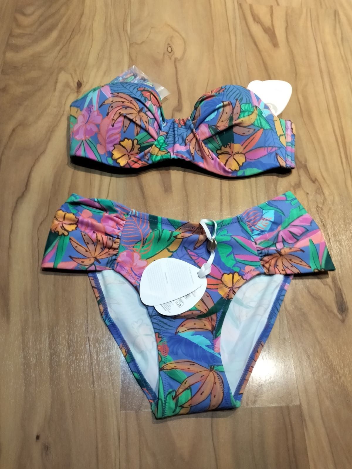 Un bikini de dos piezas de colores con estampado floral tropical sobre fondo azul, expuesto sobre una superficie de madera.
