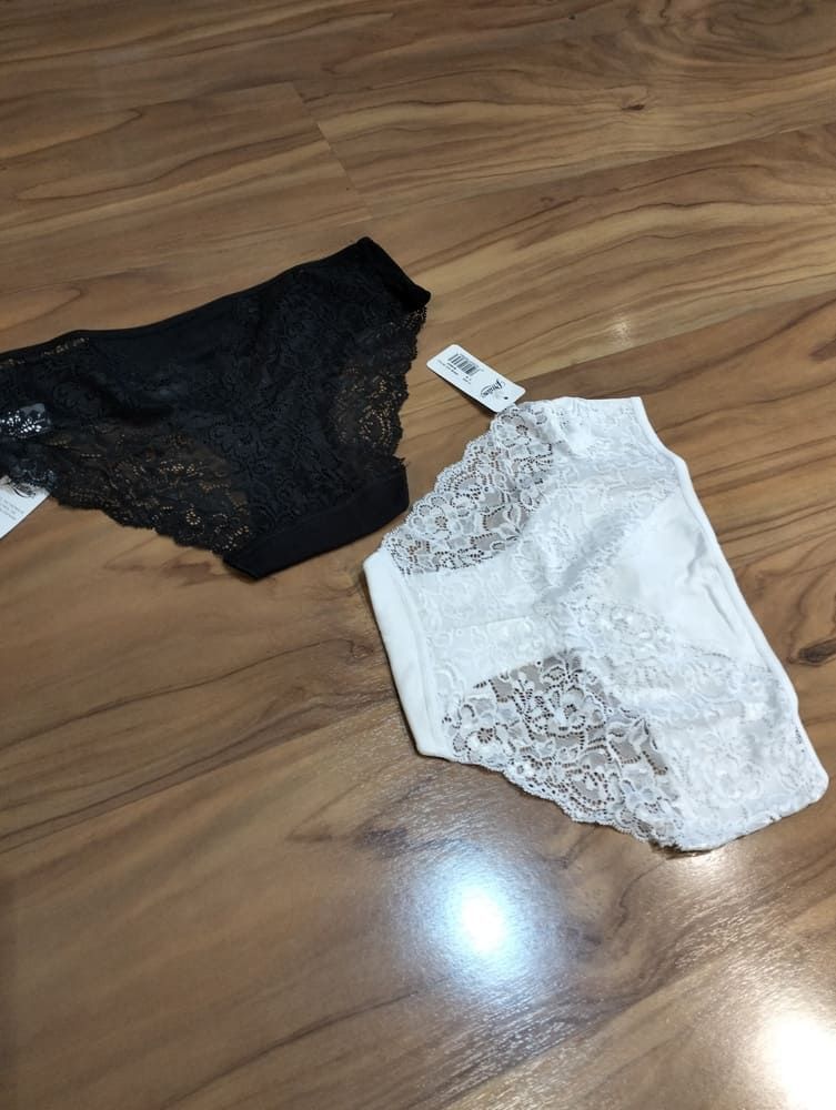 Un par de bragas negras y un par de bragas blancas de encaje con etiquetas de precio, colocadas sobre una superficie con textura de madera.