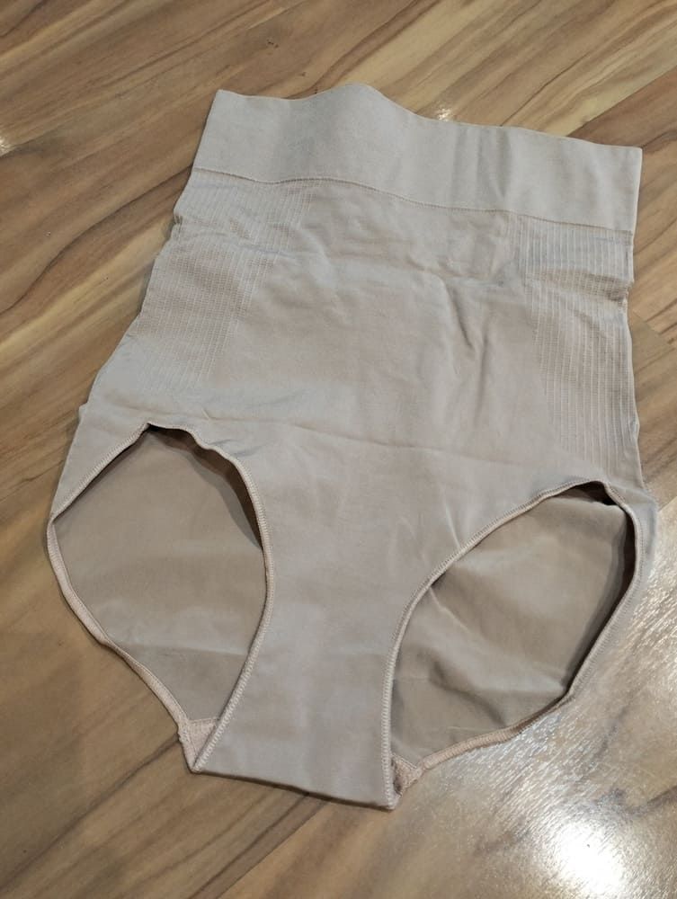 Una braguita moldeadora de talle alto de color beige yace extendida sobre una superficie con textura de madera.